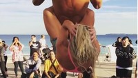 Kekuatan tubuh bagian atas yang prima membuatnya bisa melakukan chin up sembari menggendong wanita. (Foto: Instagram/MarcusBondiBeach) 