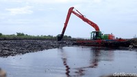 Satu buah alat eskavator berjibaku mengeruk sampah yang berlumpur.
