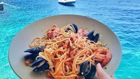 Menikmati gurihnya sepiring pasta dengan topping seafood ditemani latar pemandangan laut Santorini di Yunani yang menakjubkan. Foto: Instagram @foodintheair