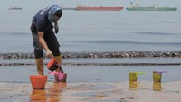 Seorang petugas kepolisian menuangkan minyak ke gayung saat membersihkan Pantai Banua Patra dari minyak yang memenuhi pesisir pantai di Balikpapan, Kaltim, Senin (2/4). ANTARA FOTO/Sheravim.