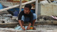 Salah satu anak kecil sedang membuat talikama layang-layang yang akan diterbangkan.