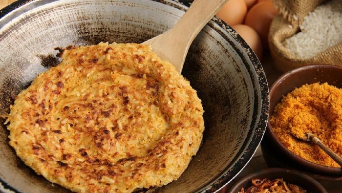 Kerak Telor, traditional food of crusty sticky rice omellete from Betawi ethnic group, Jakarta. The omelet has been cooked in a charcoal-heated metal wok; now ready to sprinkled with the dry toppings of roasted coconut and spicy shrimp mixture and crispy shallots. The toppings are placed on the right side of the wok. Further back, laid the glutinous rice grains and several chicken eggs. The image was taken outdoor in the terrace; using the afternoon sun as the main lighting source.