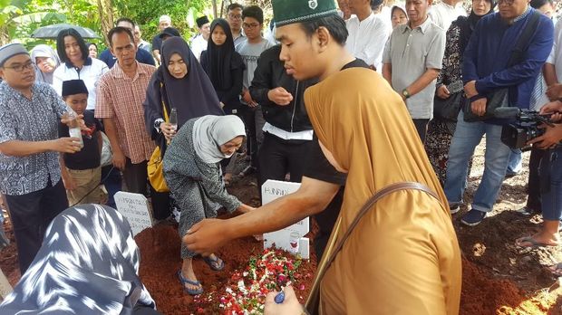 Istri Hunaidi menaburkan bunga di atas kuburan almarhum
