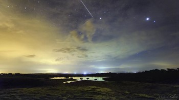 Dalam suasana mendung pada musim dingin, sebuah meteor yang bersinar terang bergerak cepat melintasi langit malam di dekat Arcturus, bintang paling terang di konstelasi Bootes. Gambar ini memperlihatkan meteor dan planet Jupiter bersinar di atas laguna kecil di Alandroal, Portugal, yang terletak di bagian utara dari Dark Sky Alqueva Reserve. Foto: Miguel Claro via Space.com