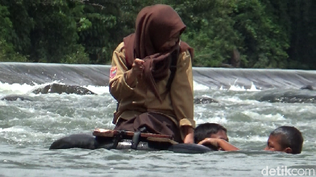 Siswa membantu siswi menyeberangi sungai menggunakan ban