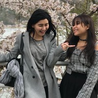 Tampil monokrom dengan kaus dan coat berwarna abu-abu, Ayu Ting Ting kembali menenteng tas Hermes seri Lindy saat berpose di antara bunga Sakura bersama adiknya, Syifa. Foto: Instagram