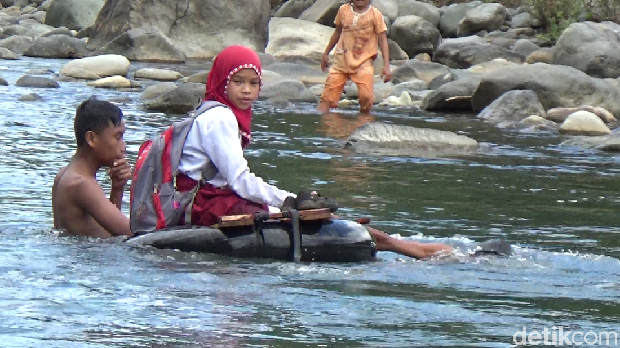 Seorang siswi menyeberangi sungai untuk bersekolah