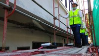 Rini yang mengenakan helm dan rompi proyek naik ke atas rangkain besi yang tersusun menjadi tangga di samping Gedung 48 Kementerian BUMN.