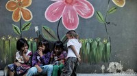 Anak-anak tengah bermain dengan latar belakang tembok bergambar bunga warna-warni.