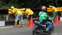 Pengendara melintas di depan pekerja yang sedang mengecat pagar flyover.