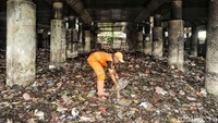 Seorang petugas mengeruk sampah yang menumpuk menggunakan cangkul.