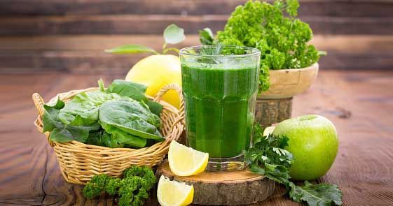 Fresh vegetable juices on wooden table, on green background