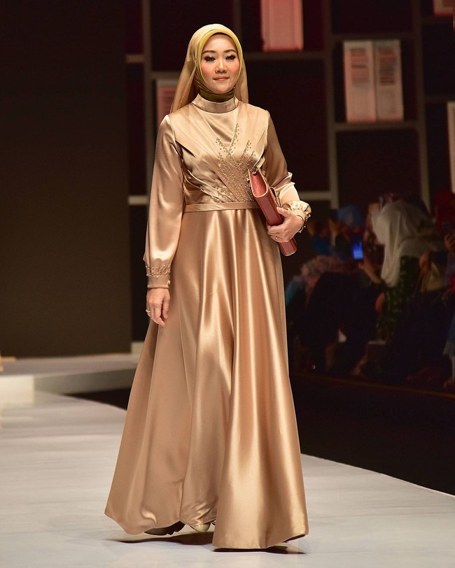 Mengenakan gaun panjang bernuansa emas metalik, Atalia melenggang di runway dengan gaya hijab modern berwarna senada. Foto: Instagram/@rya_baraba