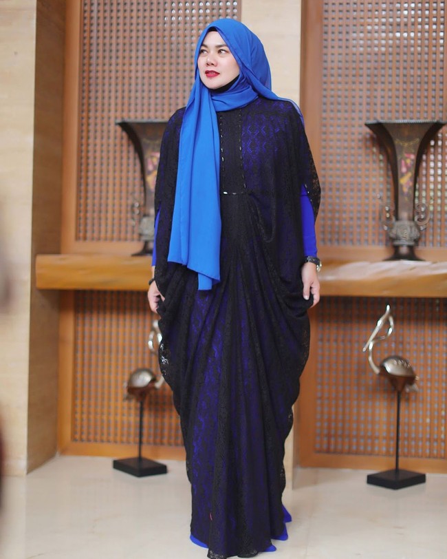 Sarita memadukan kaftan transparan berbahan lace dengan gaun panjang biru. Padu padan cerdas yang membuat pakaiannya tampak baru. Ia juga tampil cerah memakai jilbab biru muda yang senada dengan gaunnya. Foto: Instagram/@queen_saritaabdulmukti