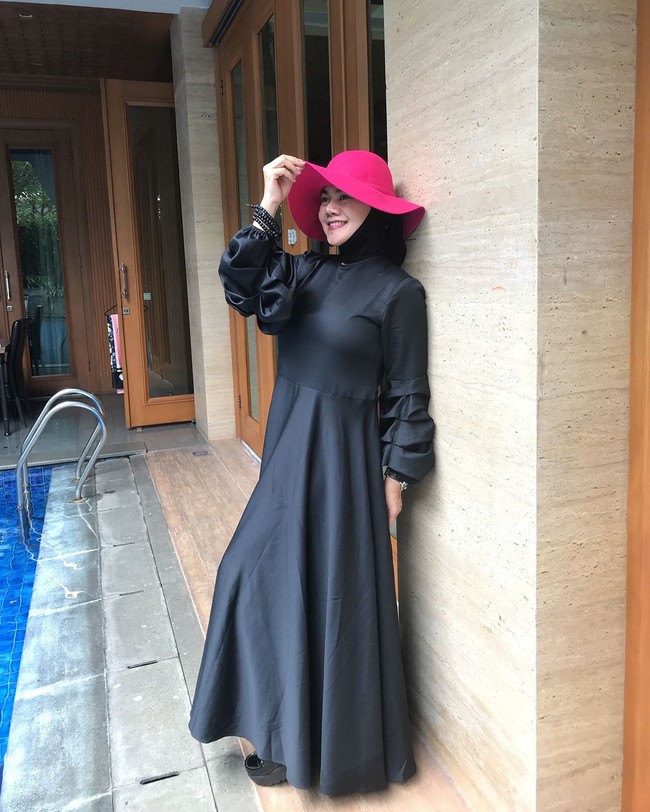 Gaya liburan Sarita Abdul Mukti dengan maxi dress hitam dan topi fuschia. Foto: Instagram/@queen_saritaabdulmukti