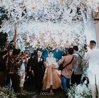 Tak terasa nuansa hutan gelap dan menyeramkan ketika resepsi dihelat di malam hari. Jalan menuju pelaminan diberi sentuhan bunga putih di kanan dan kiri, pun langit-langit yang dibuat menggantung. Dekorasi serba putih yang elegan, mengingatkan akan dekorasi pernikahan Bella dan Edward Cullen di film Twilight. Foto: Dok. Instagram/Nocture