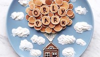 Tumpukan pancake berukuran mini ini dibuat seperti balon yang melayang di udara, lengkap dengan hiasan awan dan rumah kecil yang terbuat dari biskuit cokelat. Foto: Instagram @darynakossar