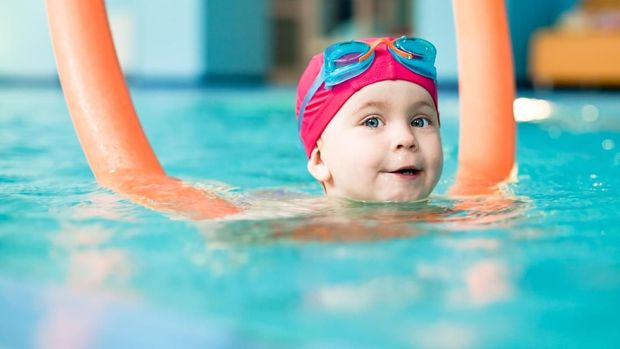 Happy little girl learning to swim with pool noodle