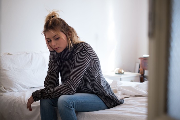 Sad young victim woman sitting on the bed at home suffering depression