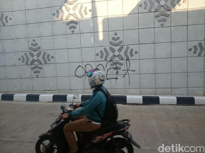 Pengendara motor memperhatikan coretan di dinding underpass Matraman, Senin (30/4/2018)