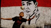 Seorang anak tampak semringah saat bermain sepakbola dengan latar belakang mural Bung Karno.