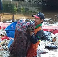 Petugas PPSU mengangkat kasur yang dibuang di sungai.