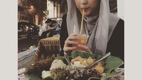 Wah, makan gudeg komplet sambil ditemani dengan segelas es buah memang enak. Apalagi makannya sambil duduk lesehan. Gaya April saat minum terlihat anggun. Foto: Instagram @apriljasmine85