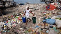 Terlihat seorang nelayan sedang memikul ember berisikan ikan hasil tangkapannya di laut yang penuh sampah. Jes Aznar/ Getty Images.