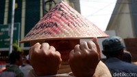 Seorang pendemo dengan memakai caping melakukan aksi borgol tangan dengan borgol plastik.