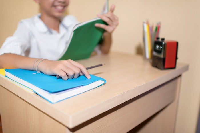 ilustrasi anak sekolah A Happy Little Asian boy holding pencil while reading on notebook homework with smiling face on wooden table.Back to School concept.