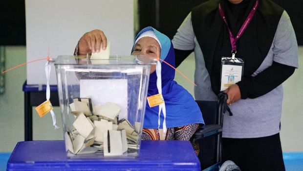 Salah satu warga Malaysia yang berkursi roda memasukkan surat suara ke kotak suara usai memilih