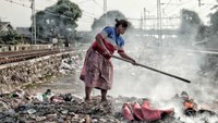 Seorang ibu sedang membakar sampah di pinggir rel kereta api.