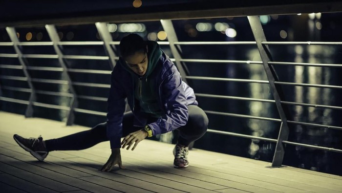 Woman stretching after jogging. River and city lights in the background. Toned image