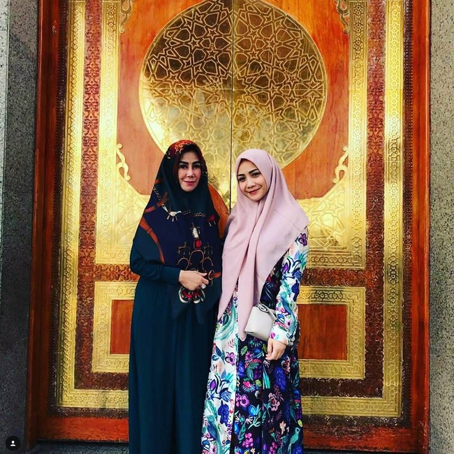 Berfoto bersama sang mertua, Nagita Slavina tampil cantik dengan dress bermotif floral dan hijab segi empat polos yang dijulurkan hingga ke bawah. (Foto: Istimewa)