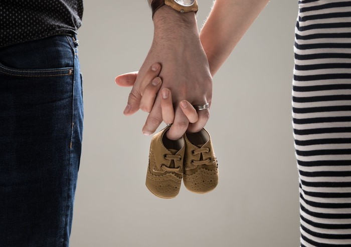 ilustrasi kehamilan A couple of adults holding a pair of baby shoes.