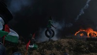 Seorang pemuda Palestina memegang ban sementara lainnya berlindung dari tembakan gas air mata tentara Israel. Foto: Ibraheem Abu Mustafa/Reuters