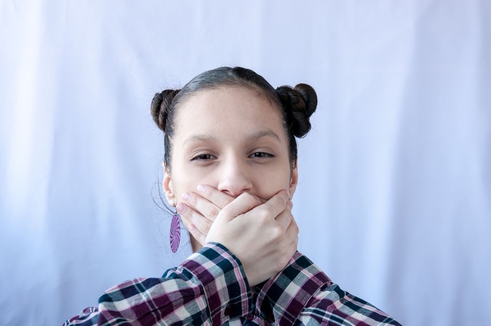 A teenage girl in a plaid shirt covered her mouth with her hands