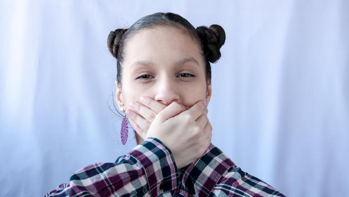 A teenage girl in a plaid shirt covered her mouth with her hands