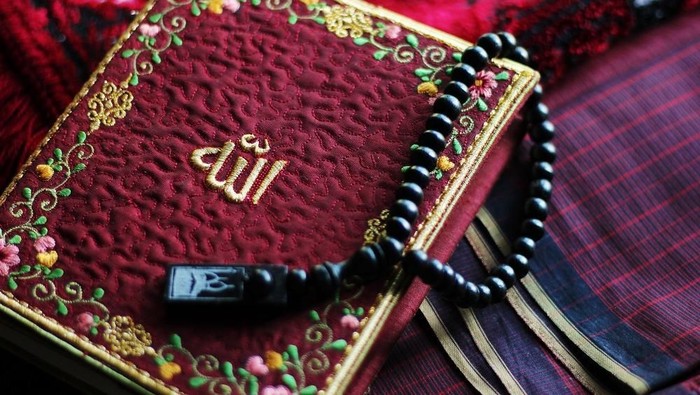 Holy Al-Quran with Allah name on it embraced with beads.