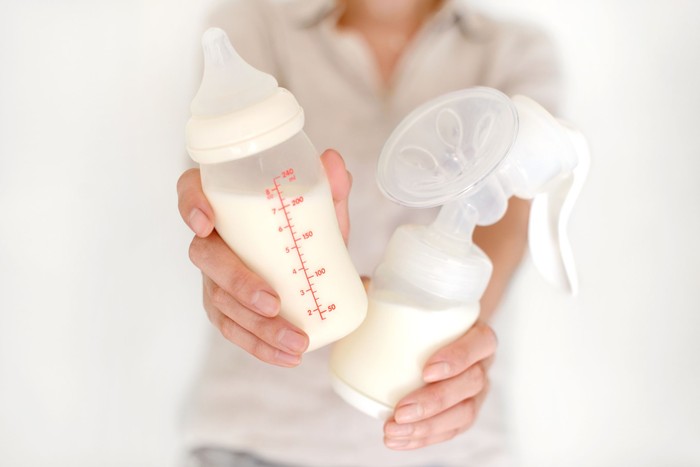 ilustrasi pumping asi Breast pump and bottle with milk in womans hand in blurred background