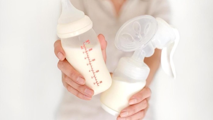 ilustrasi pumping asi Breast pump and bottle with milk in womans hand in blurred background