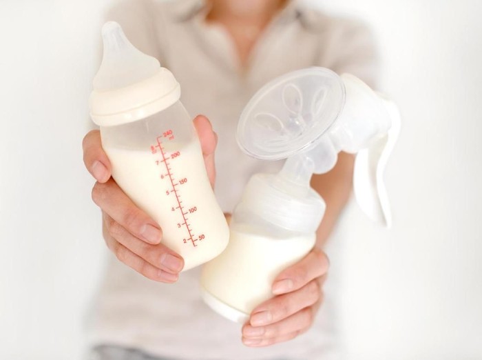 Breast pump and bottle with milk in womans hand in blurred background