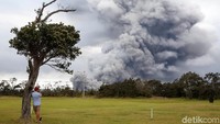 Sambil bersandar di sebuah pohon, seorang warga mengabadikan letusan gunung. REUTERS/Terray Sylvester.