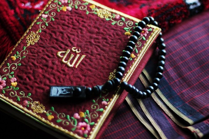 Holy Al-Quran with Allah name on it embraced with beads.