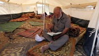 Beberapa warga Palestina menyambut bulan Ramadan di tenda-tenda pengungsian. Seorang pria sedang membaca Al-Quran selagi menunggu waktu berbuka puasa. Ibraheem Abu Mustafa/Reuters.