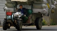 Seorang pria mengendarai sebuah traktor yang membawa tumpukan karung beras di Huaian.