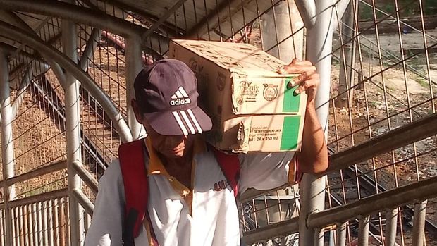 Warga memanggul kardus sambil menaiki anak tangga JPO