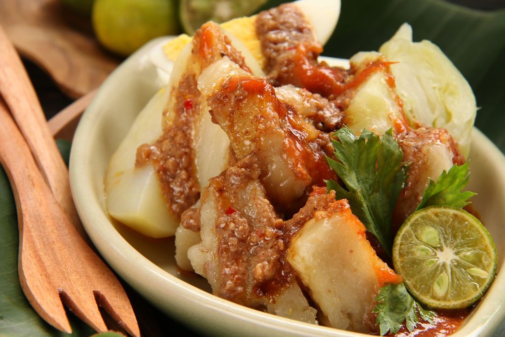 Siomay Bandung, popular Sundanese snack of steamed fish dumplings, potato, cabbage roll, and egg. Served with variety of condiments as spicy peanut sauce, chili sauce, and sweet soy sauce. A squeeze of lime is also added just before eating. This snack is plated on a oval-shaped ceramic plate; placed on a banana-leaf-lined wooden plate. Two small wooden forks are placed aside. This image was taken outdoor and used afternoon sun as the lighting source.