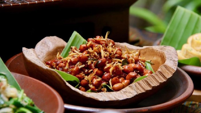 Kacang Teri, a popular Balinese and Javanese side dish of fried peanuts and anchovies with palm sugar and chili dressing. Served in teak-wooden bowl lined with banana leaf; then placed on an earthenware plate.
