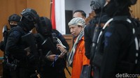 Kedua tangan Aman juga diborgol polisi. Namun saat berada di arena sidang borgol itu dilepas.